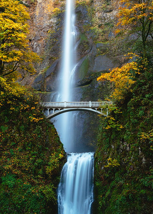 a flowing waterfall behind a small bridge