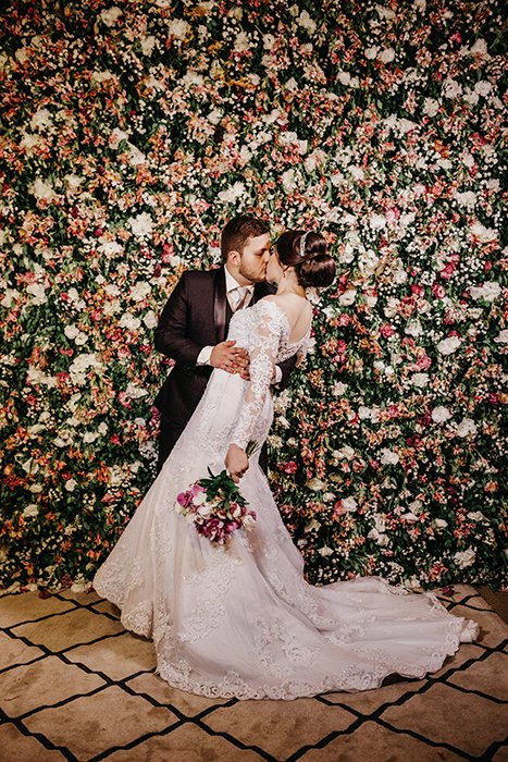 A bride and groom kissing in front of a floral wall 