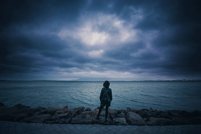 A person standing in front of a lake with dark skies 