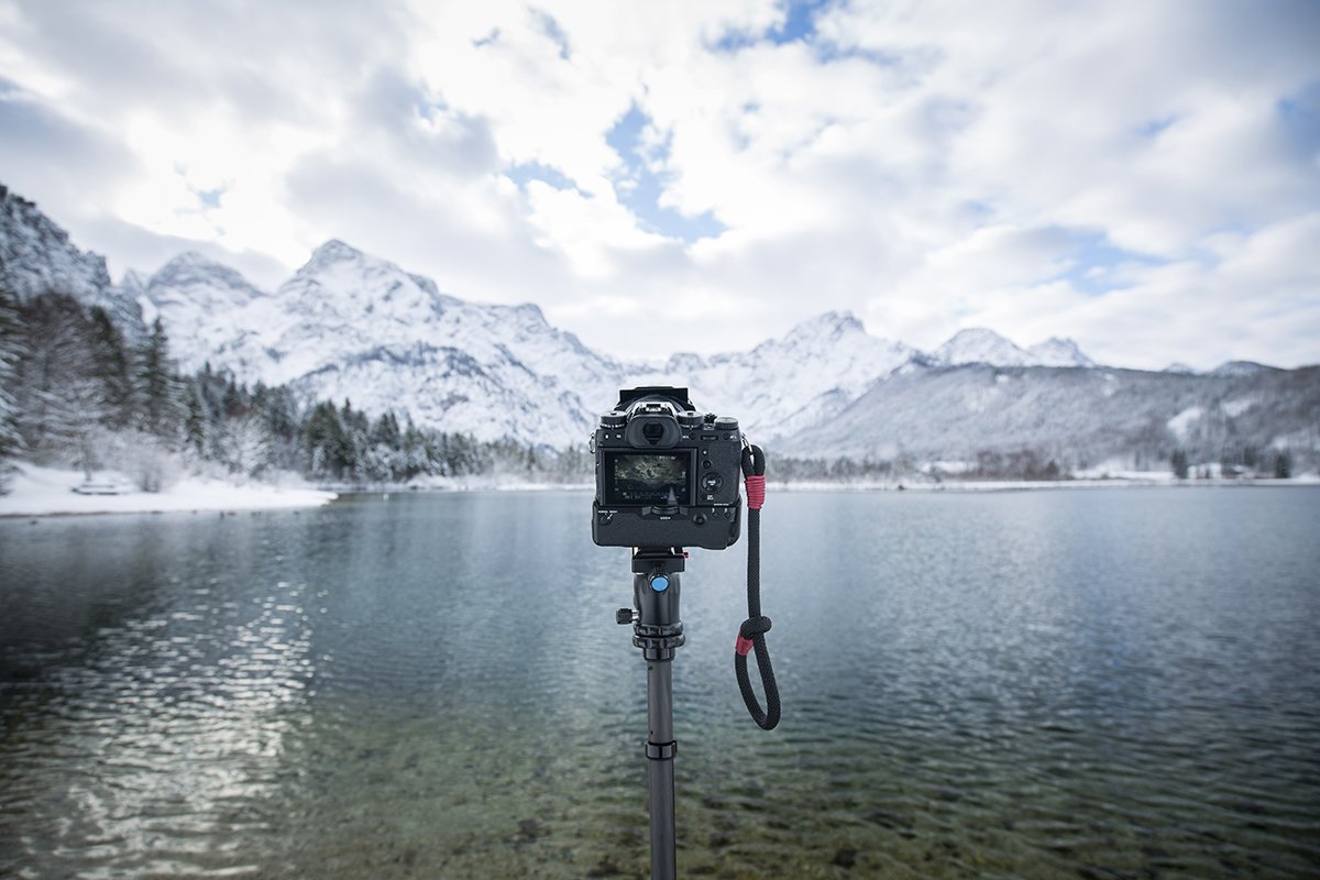 A camera set up on a tripod in front of a snowy mountain and lake for day-to-night time-lapse photography