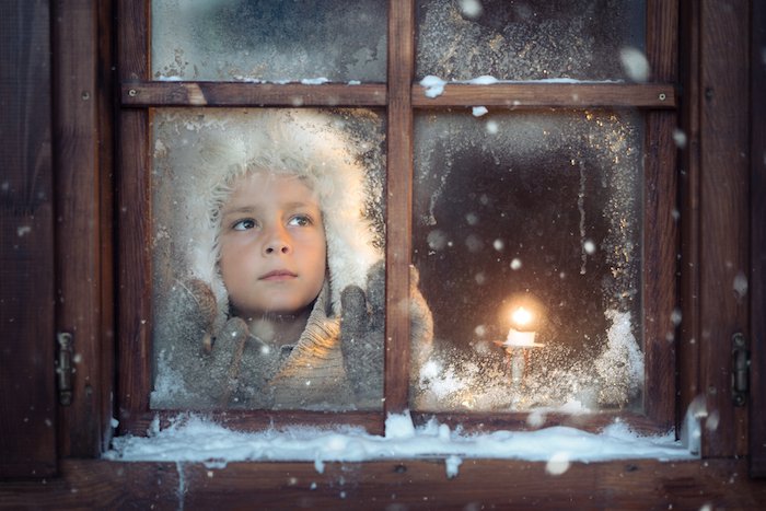 child looking outside a window in winter with a candle beside them