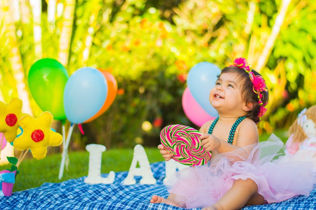 A toddler holding a giant lollipop while sitting on a blanket for a kids photo pose