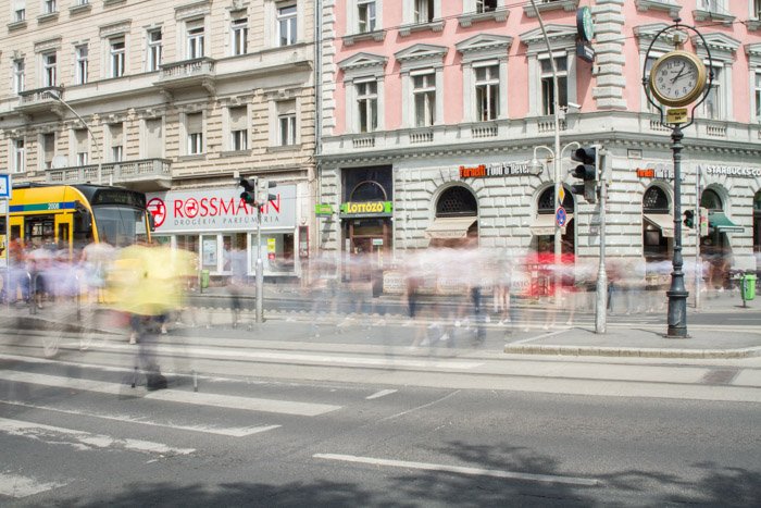 A picture of a city street with blurry people walking across an intersection in front of a building