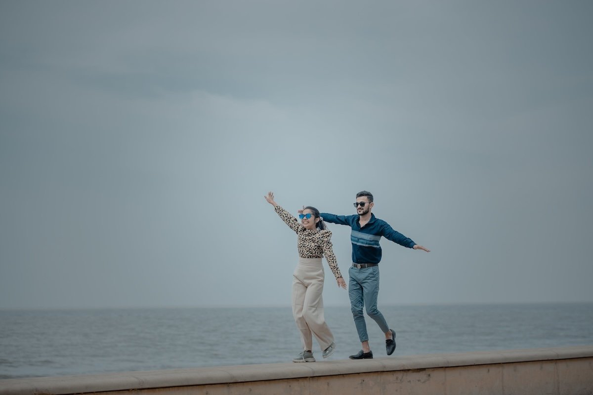 Two people pretending to balance on a wall beside the ocean for couple poses