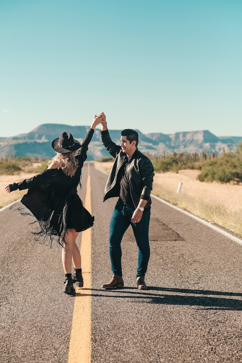 Two people dancing on a desert highway in matching western outfits for couple poses