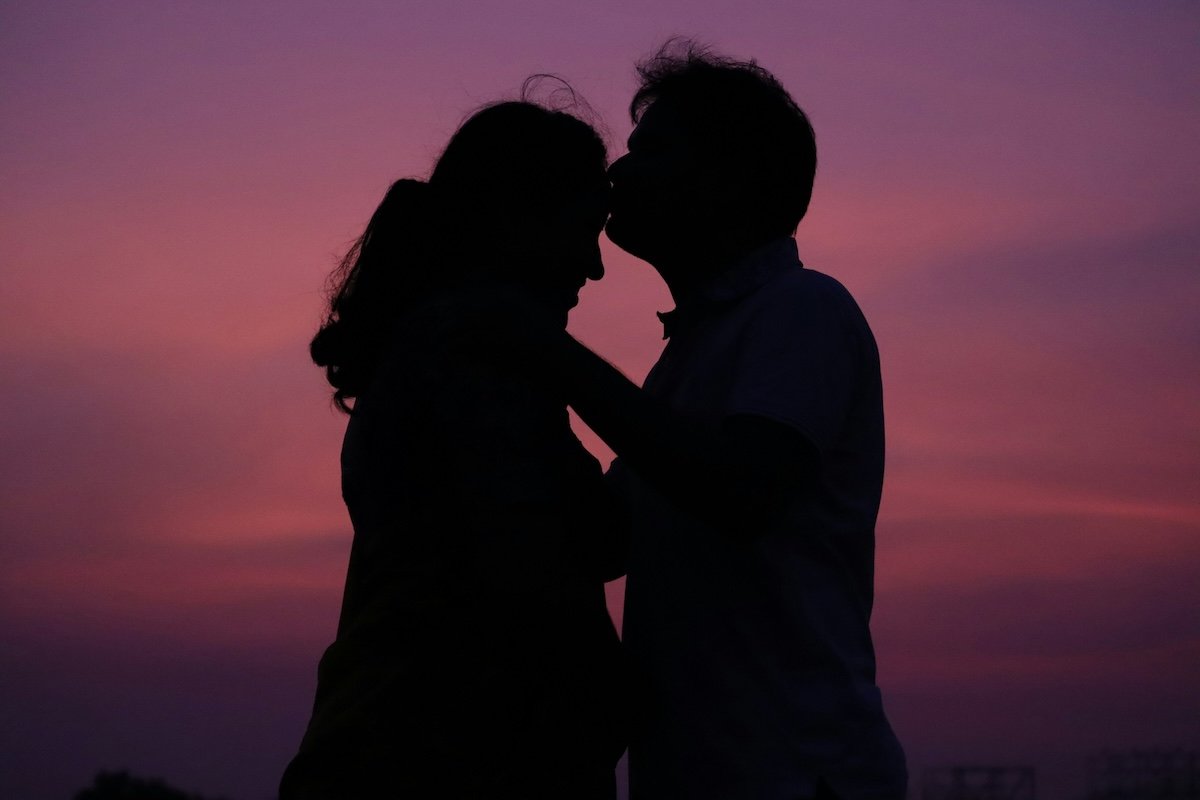 Silhouette of couple at dusk of a man kissing a woman's forehead for couple poses