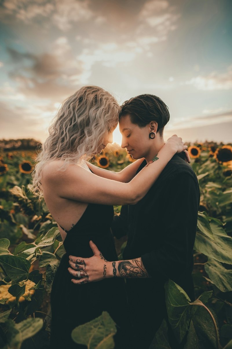 Two women in a sunflower field standing with their foreheads touching for couple poses