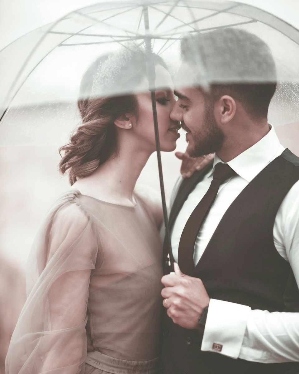 Two people kissing under an umbrella in the rain for couple poses