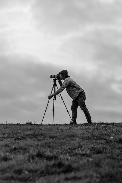 A man taking a shot through a DSLR on tripod in a gloomy landscape