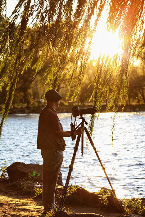 A photographer setting up a shot with a camera and tripod by a lake