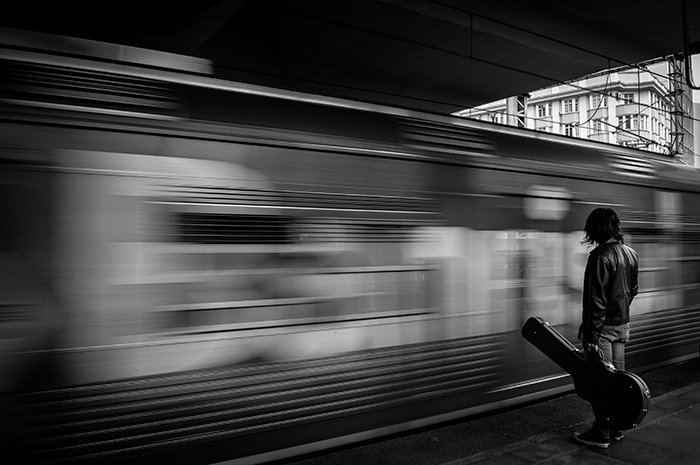 a person with guitar case standing by a moving train
