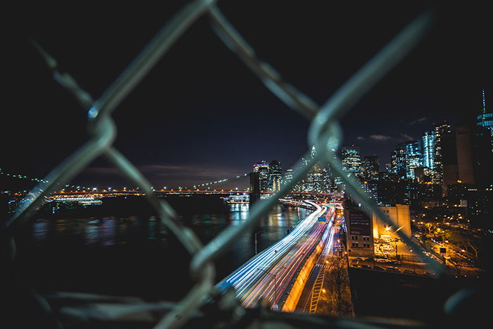 Night cityscape shot through a chain link fence