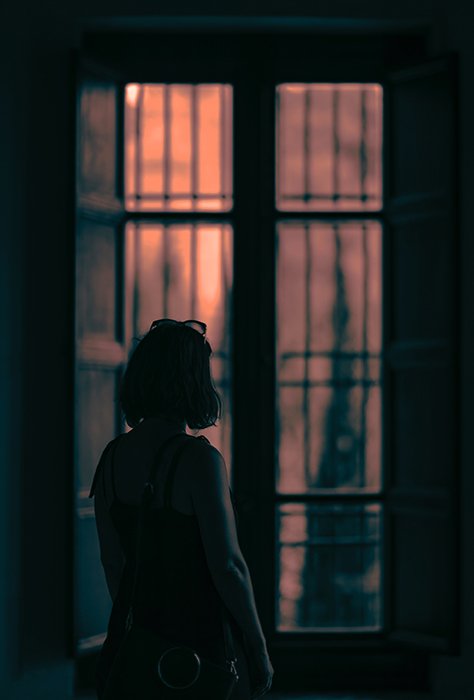 Moody scene of a girl looking out a window in a dark room