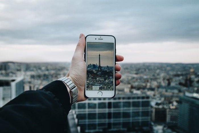 A hand holding up a smartphone camera to take a picture of the Eifel tower up high above buildings