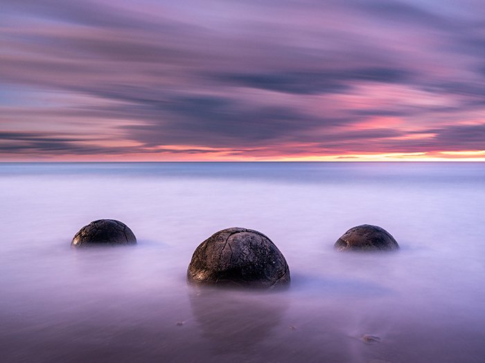 boulders in the sea under a long-exposure sky