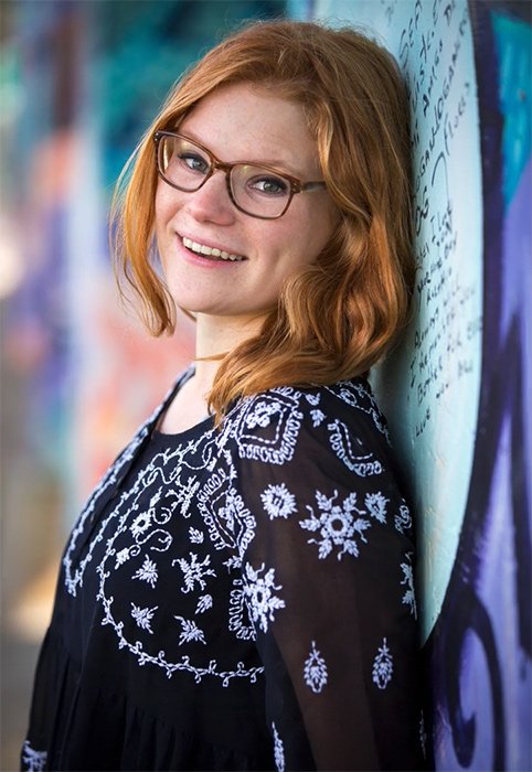 Portrait of a woman with glasses smiling and leaning against a wall 