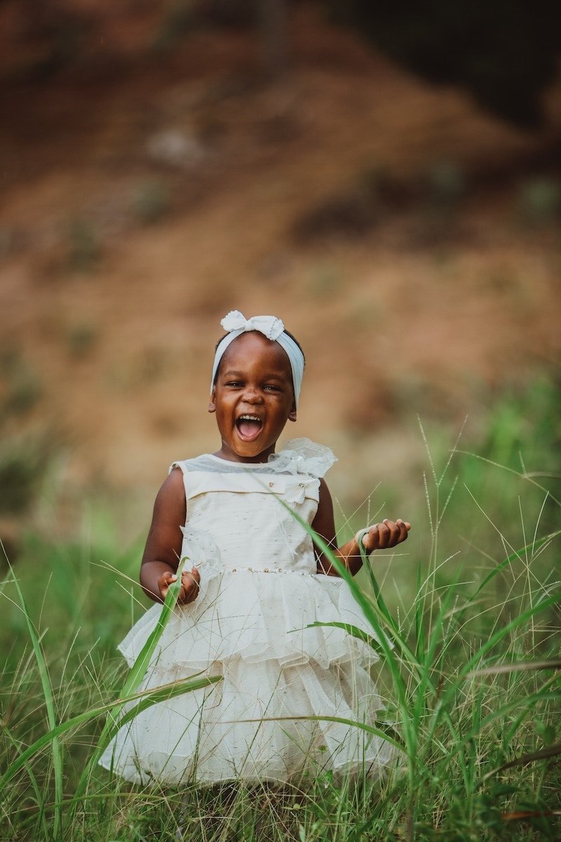 Toddler in a white dress standing in tall grass