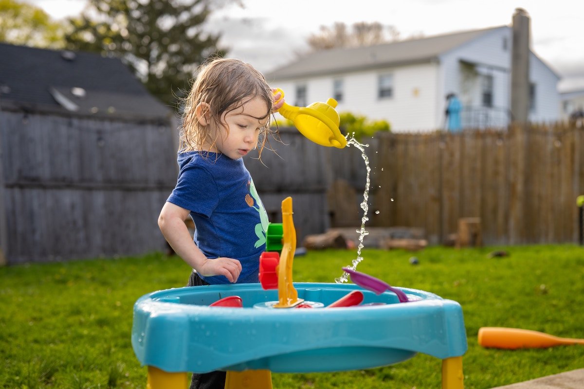 A toddler playing with water toys in a yard