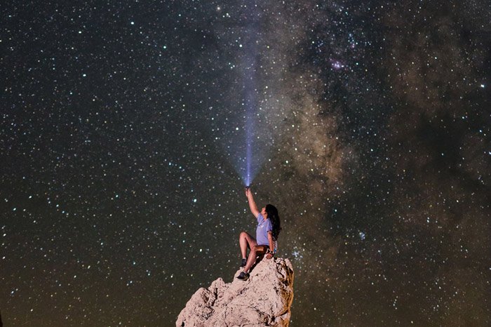 A girl sitting on a cliff with the Milky Way above her