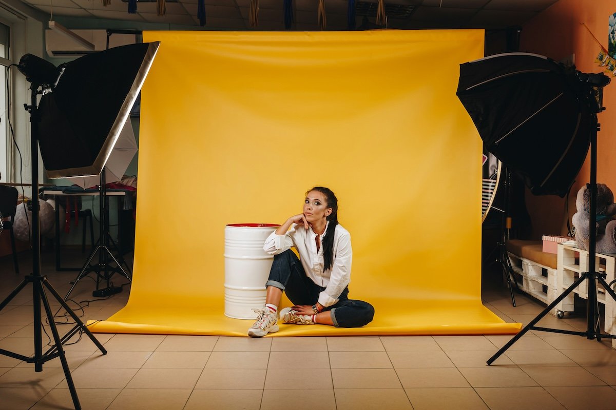 A woman posing in front of a yellow backdrop for a photoshoot for how to make money with photography