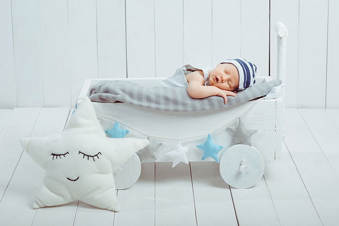 Portrait of adorable infant baby in hat sleeping in wooden crate.