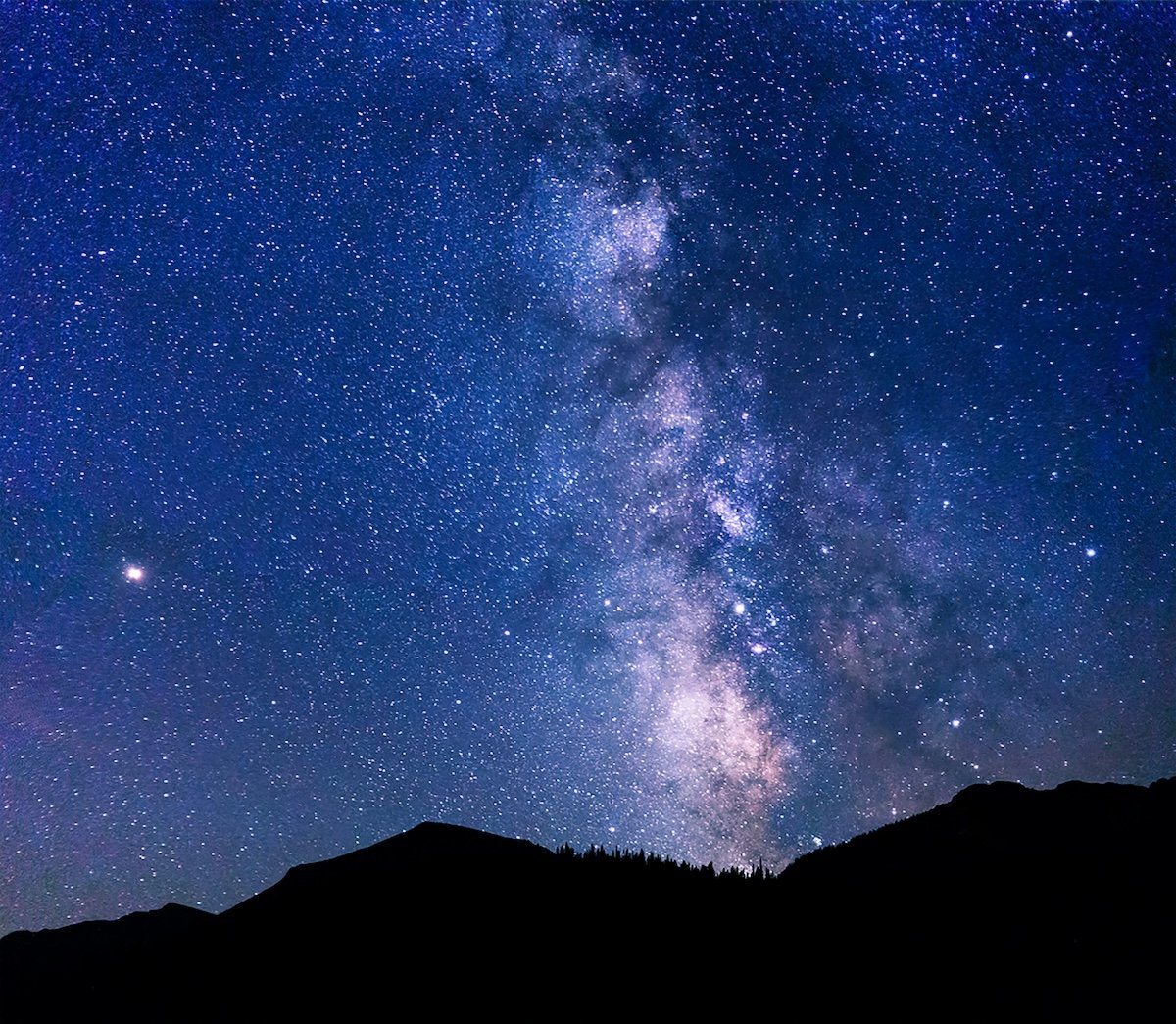 A night sky time-lapse photo of the Milky Way with a mountain silhouette