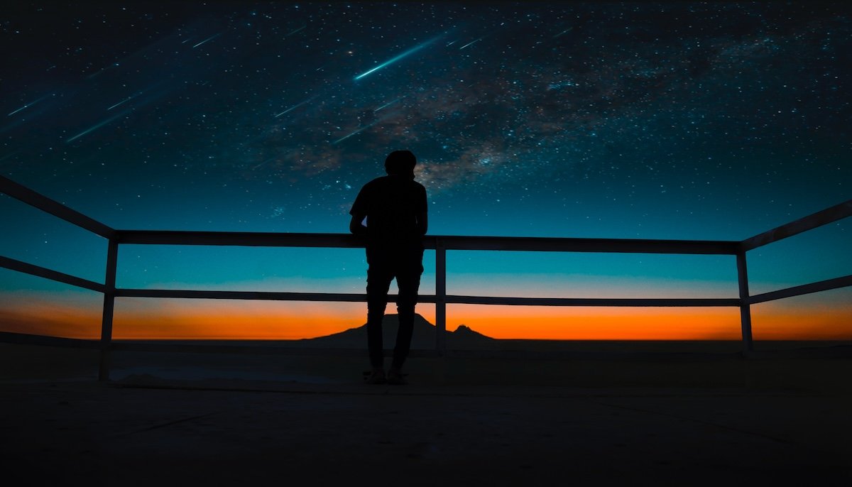 Silhouette of a person against a night sky time-lapse photo with a colorful dusk sky and shooting stars