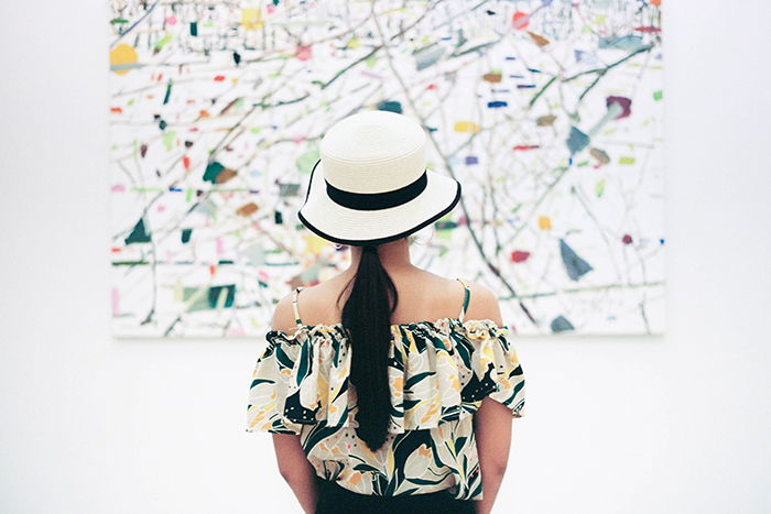 A girl in a white and black hat looking at an abstract painting