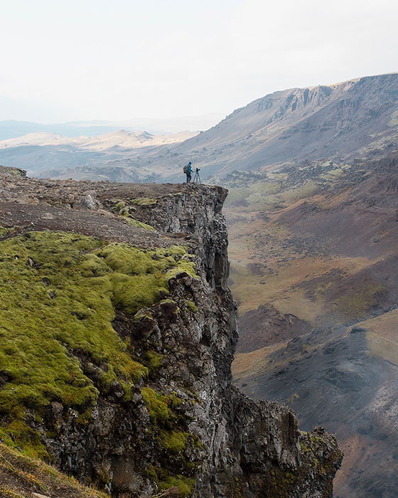 A photographer setting up a camera on the edge of a cliff