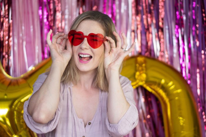 Portrait of women in heart sunglasses against a DIY photo backdrop made of party streamers