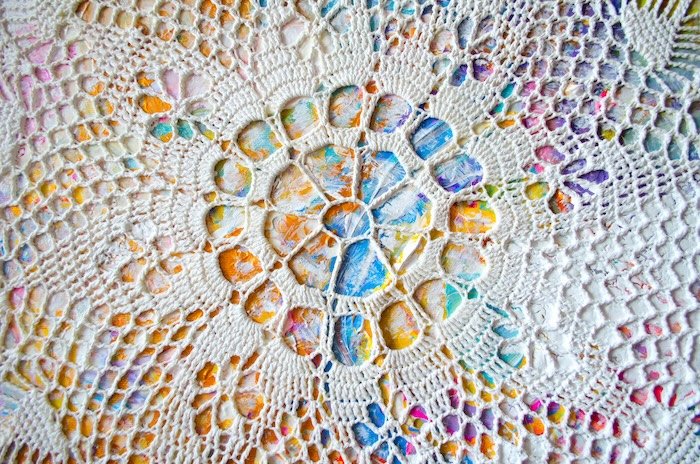 A doily laid over a colorful painted canvas for a DIY photo backdrop