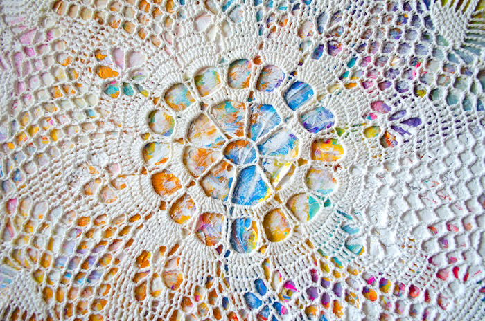 A doily laid over a colorful painted canvas for a DIY photo backdrop