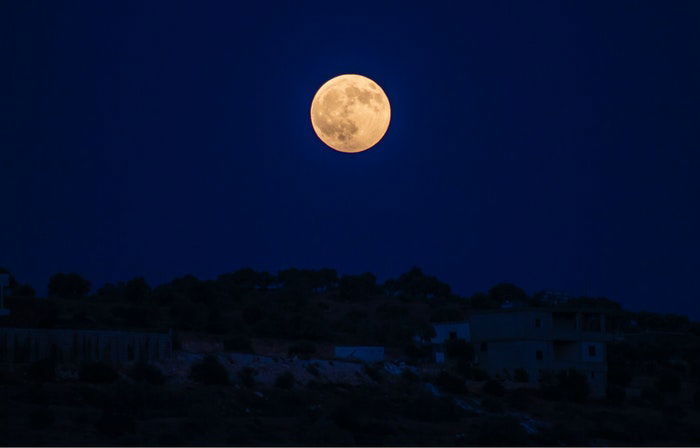 Photo of the full moon above a town at night