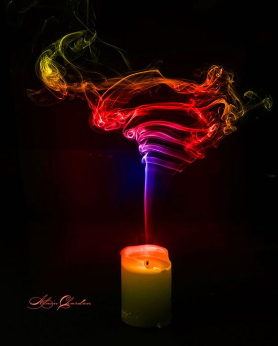 A vivid candle is being blown out by a swirl of rainbow-colored smoke. 