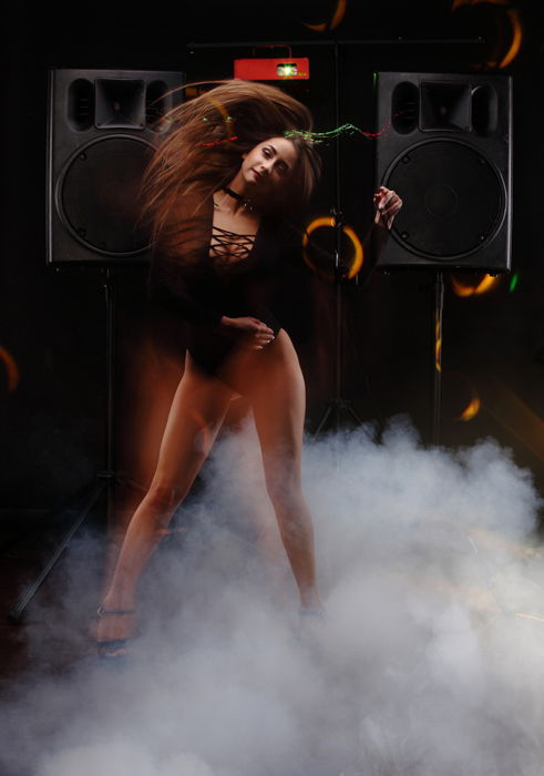 Woman dancing in a studio with two loudspeakers in the background. 