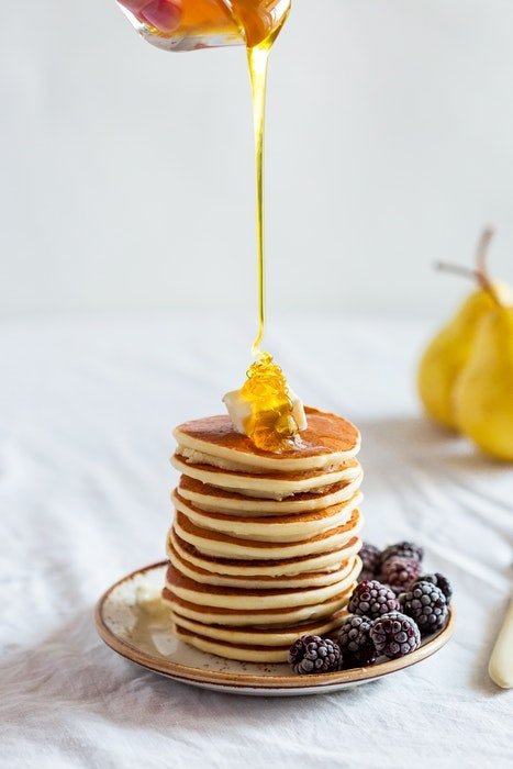 A hand pouring syrup on top of a stack of pancakes
