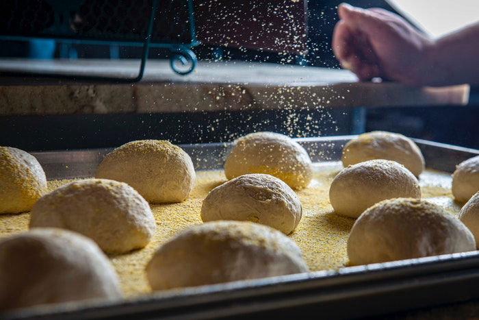 Sprinkling flour onto balls of dough in a baking tray