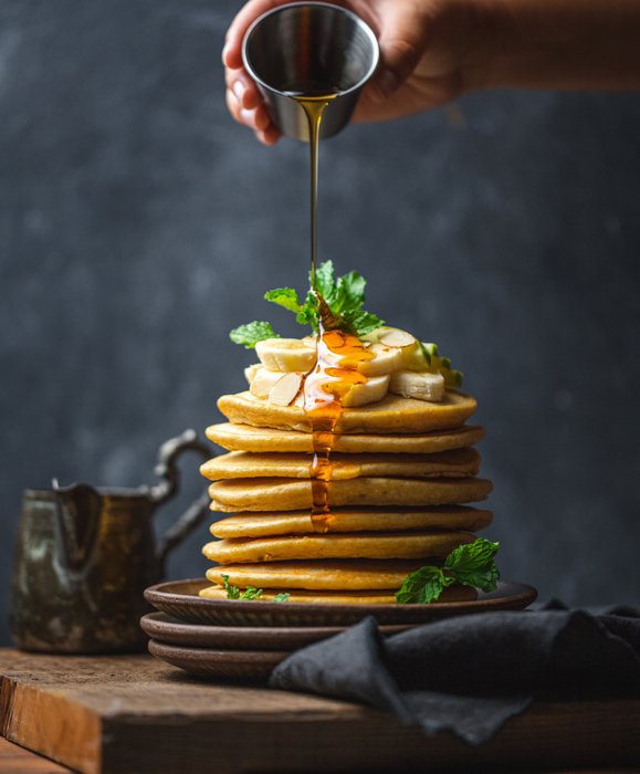 A hand pouring syrup on top of a stack of pancakes