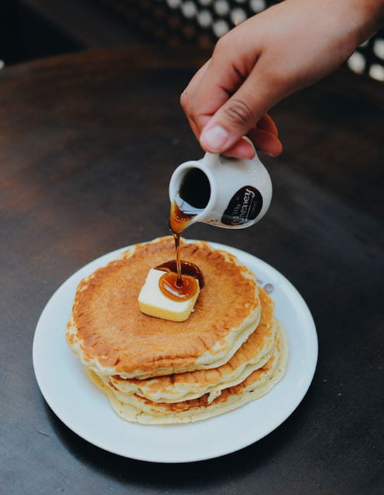 A hand pouring syrup on top of a stack of pancakes