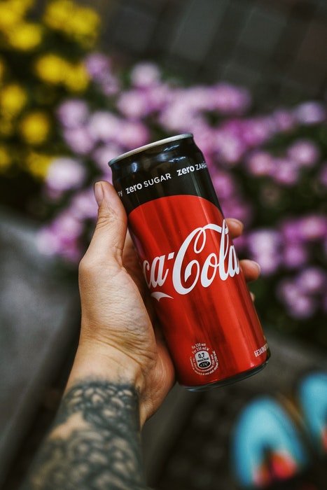 A food commercial photo of a hand holding a coca cola against a floral background