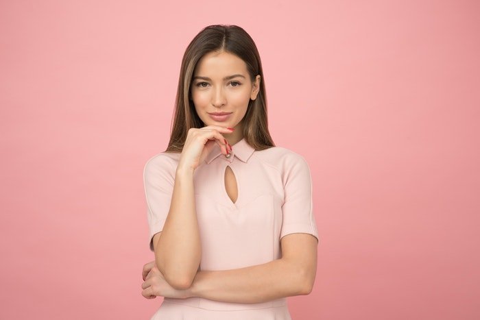 Woman in front of a pink background demonstrating a hand pose 