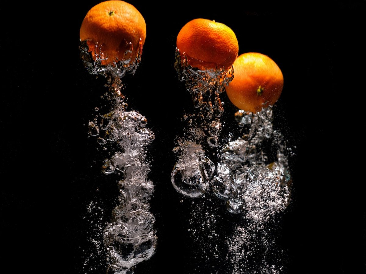 Inverted image of oranges splashed in water against a black backdrop for high-speed photography