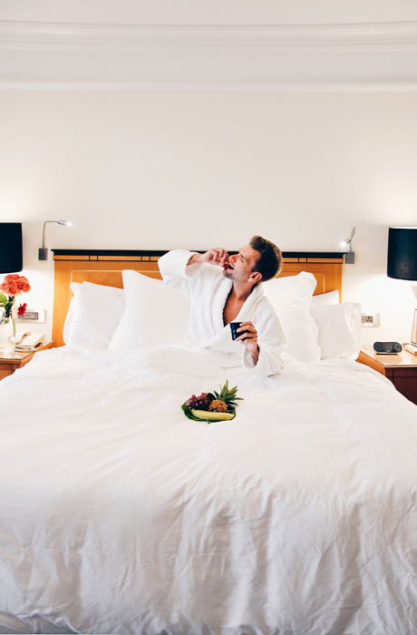 A man in a hotel bed eating from a bowl of fresh fruits