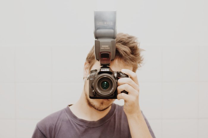 Photo of a guy holding a camera with external flash in front of his face