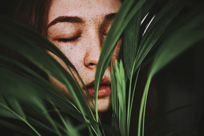 Una niña posando en el interior cubierta por plantas.