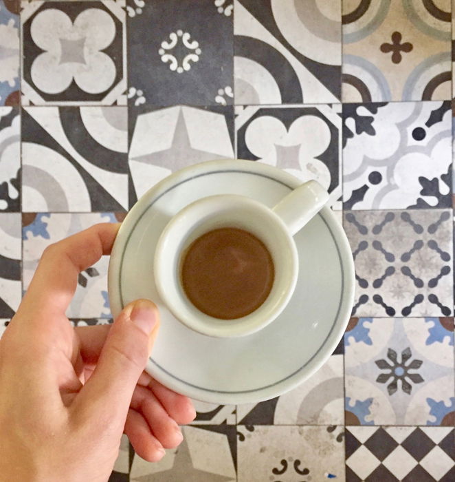 A person holding a teacup over patterned tiles