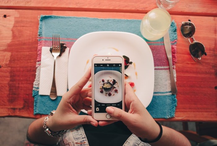 Hands holding an iPhone above a plate of food for smartphone photography
