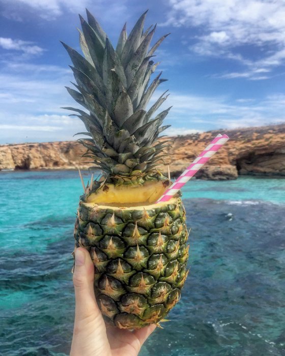 Cool iphone food photography of a hand holding a pineapple cocktail to a seascape
