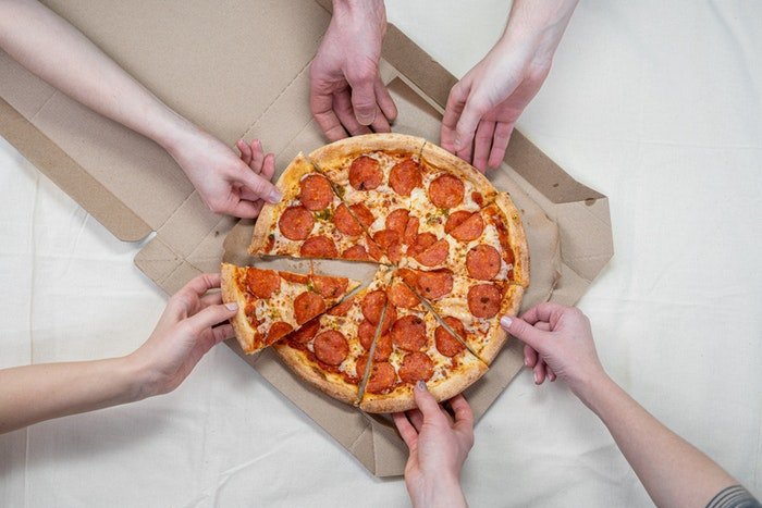 Overhead shot of people grabbing pizza slices from a box