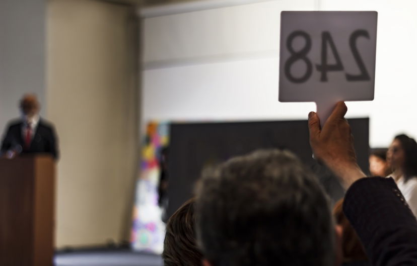 A raised hand with a number on a sign for an auction for the most expensive photographs